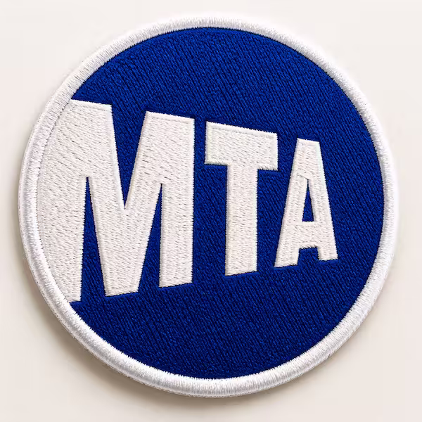 Round blue embroidered patch displaying large white MTA letters for the transit authority