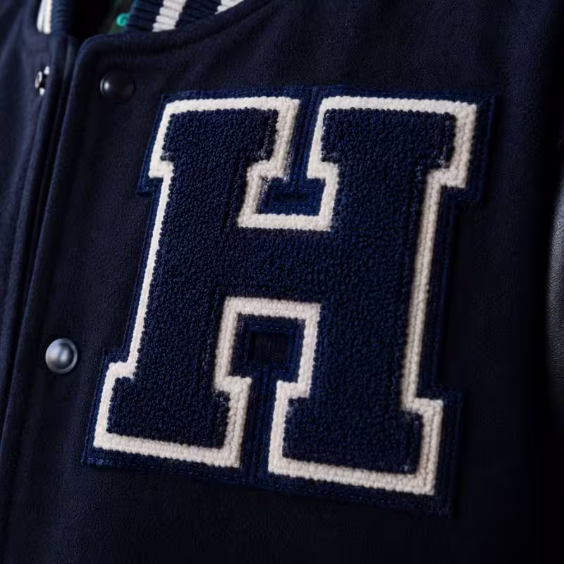 Large navy blue and white chenille letter H patch sewn onto a classic varsity jacket