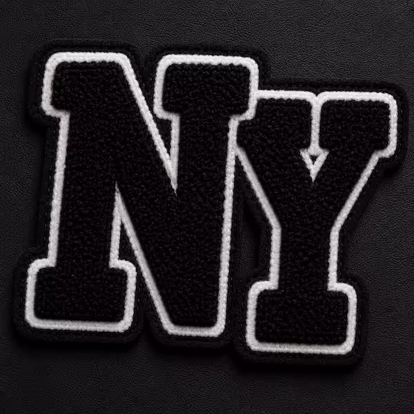 Black chenille patch featuring the letters NY with a white stitched border outline on a dark surface