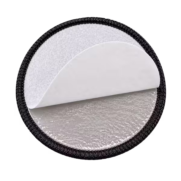 Back of a round patch with a white paper liner peeled back showing sticky adhesive backing