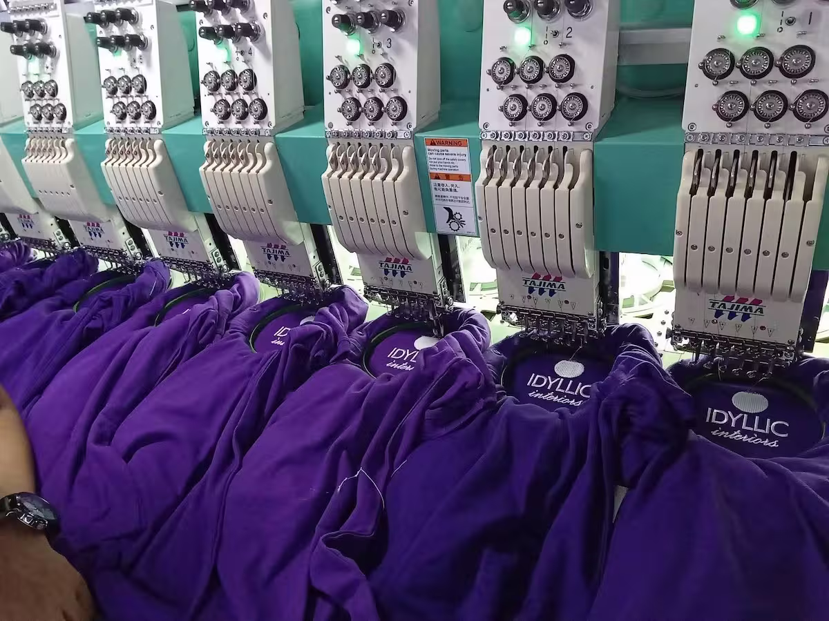 Tajima commercial embroidery machine stitching custom white embroidered patches onto multiple purple hoodies