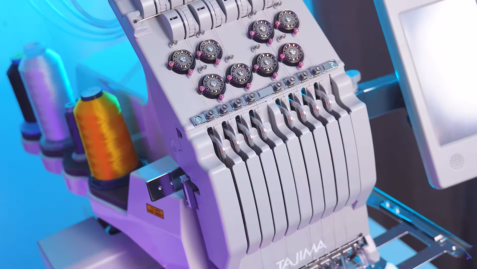 Close up of a modern Tajima multi needle embroidery machine with bright thread spools under blue lighting